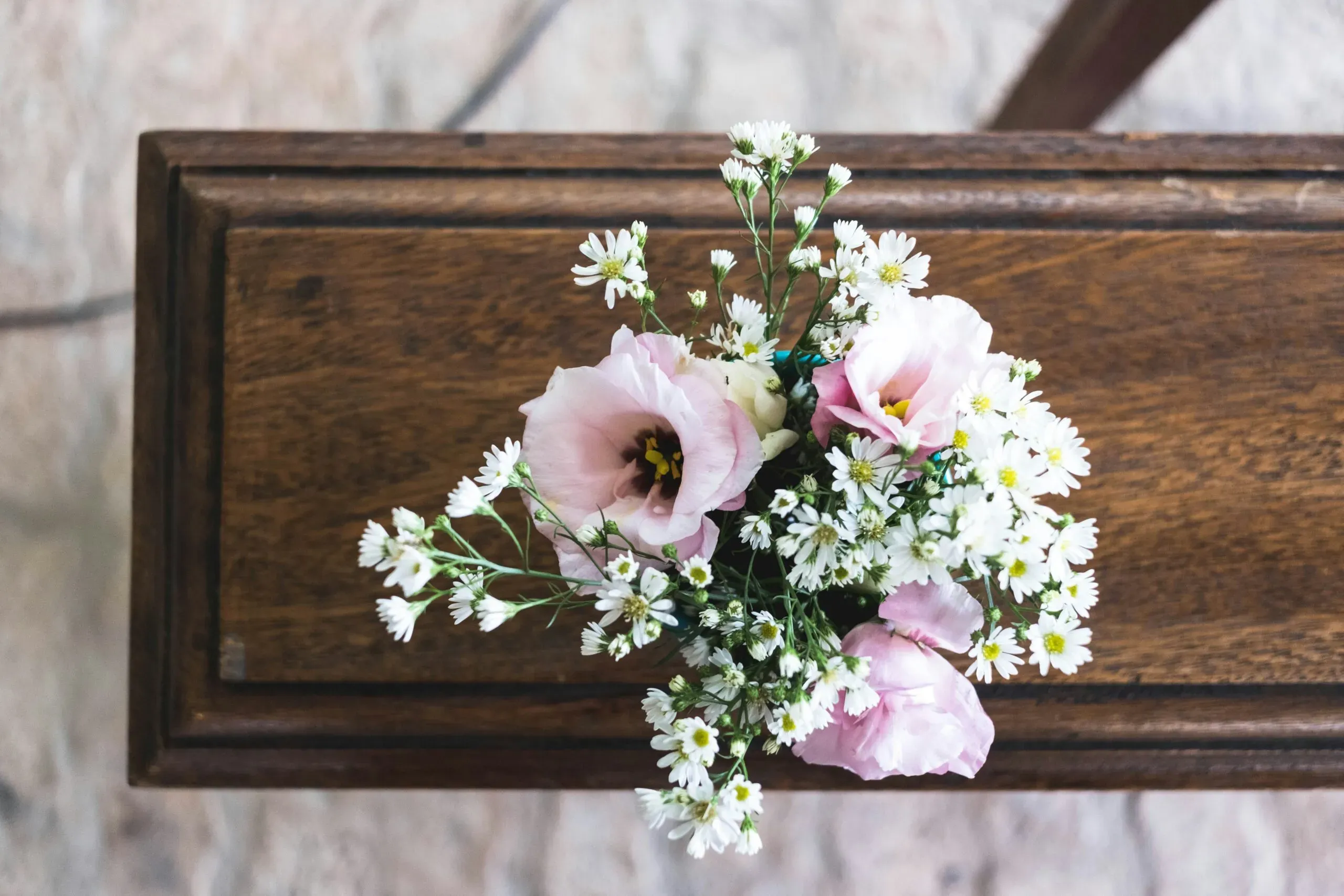 Petit bouquet de fleurs roses et blanches déposé sur un cercueil en bois.